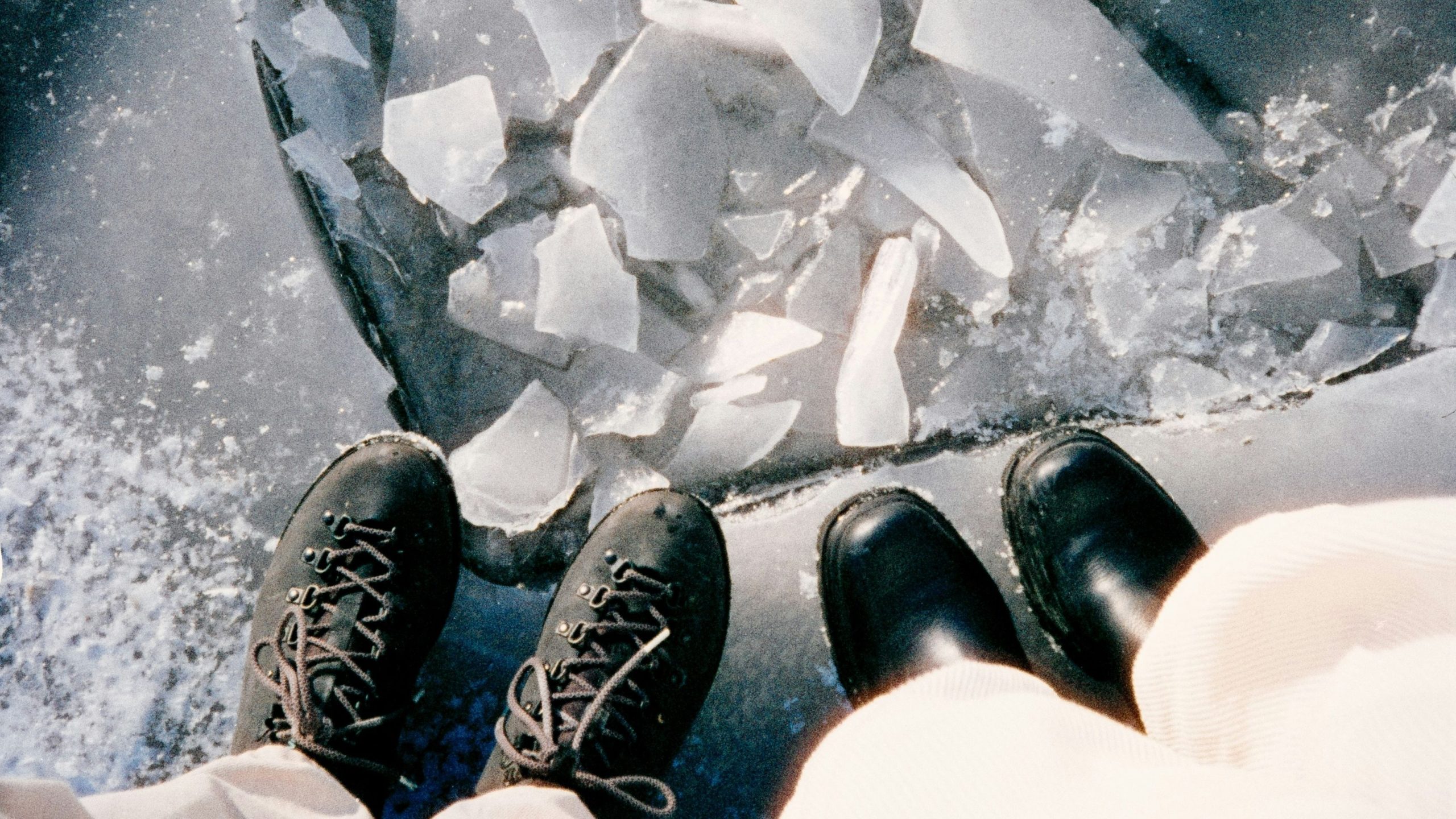Close up of two people's boots at the edge of an ice pool. (Janke Laskowski/unsplash)