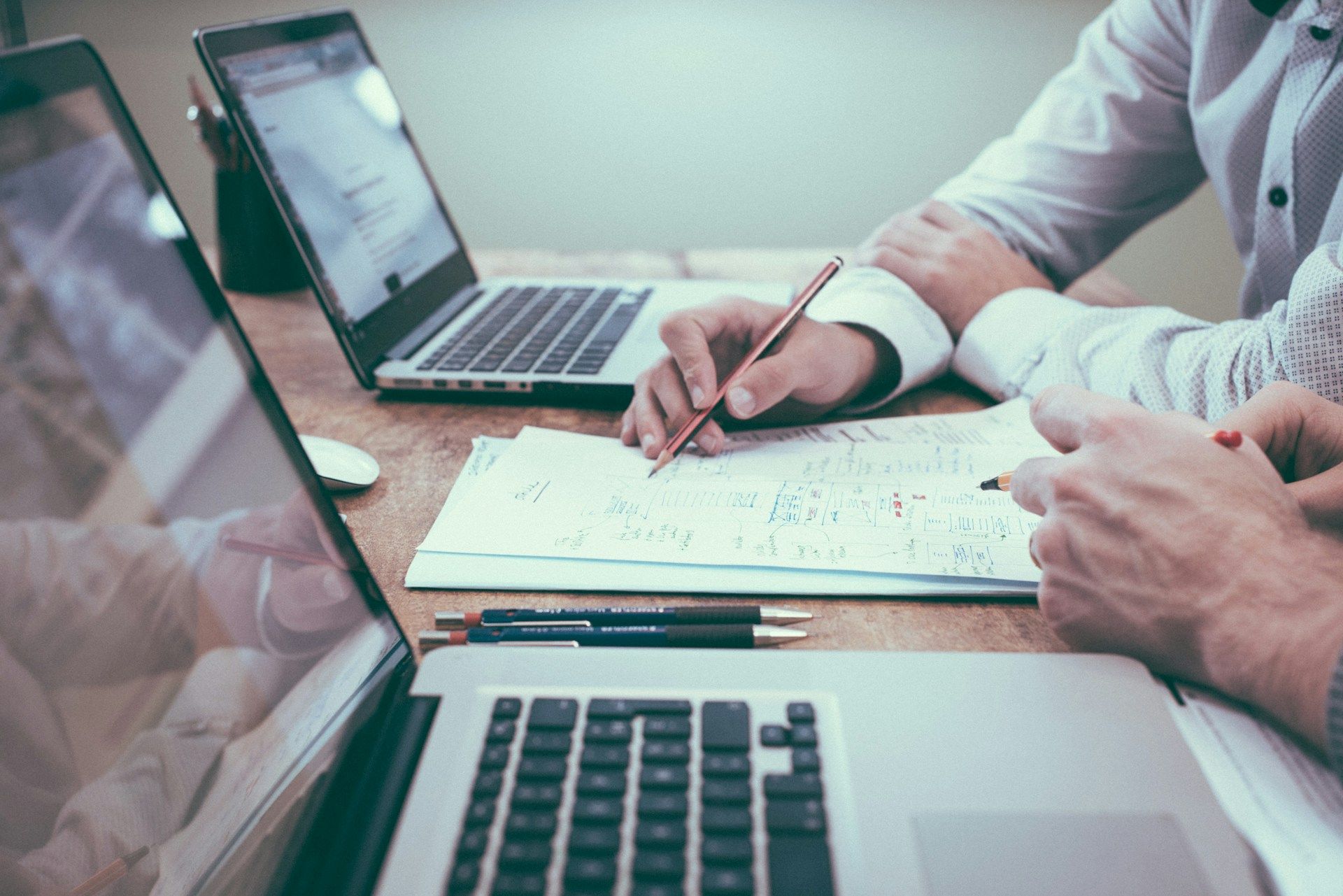 Two people work on a paper document surrounded by laptops.